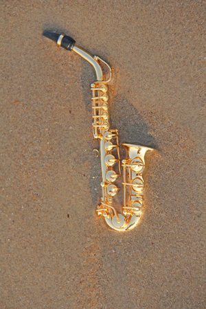 The golden alto saxophone lies on the sand or on the beach. Musical cover and creative. Design with copy space.の写真素材