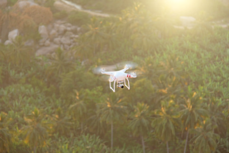 Quadrocopter drone white flying over the palm jungle of Hampi, India.の写真素材