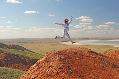One girl jumps up in nature, on a mountain, against a blue sky backgroundの写真素材