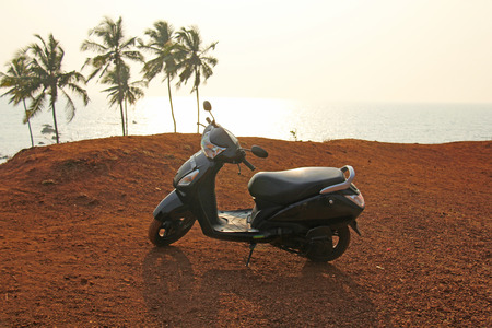 Black scooter stands on top of the mountain against the background of the sea and palms, India, GOA.の写真素材