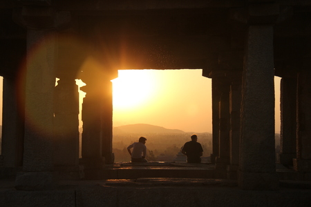 Two silhouettes of men on a sunset background in Hampi, India. Not far from the temple of Ganesha.の写真素材