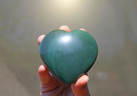 The hand holds the heart from natural stone green jade. Heart in hand. A stone in the shape of a heart. Love talisman, zen, spa.の写真素材
