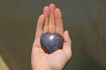The hand holds the heart from natural stone. Heart in hand. A stone in the shape of a heart. Love...
