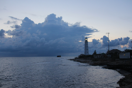 A lighthouse against a background of beautiful blue and large clouds. A lighthouse at night, a beacon signal on the seashore.の写真素材