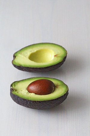 Avocado on a white wood background. Two halves of avocado and kernel, nut. Vegetarianism and healthy...