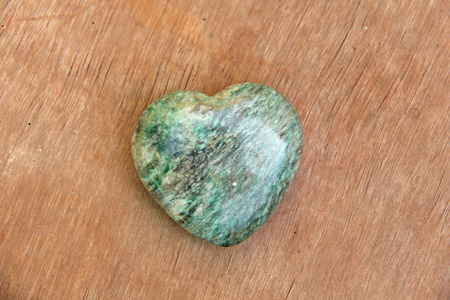 Green heart made of natural stone marble. A heart shaped stone lies on a brown or beige background....