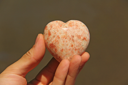 The hand holds the heart from natural stone rhodochrosite. Heart in hand. A stone in the shape of a heart. Love talisman, zen, spa.の写真素材