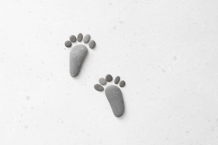 Footprints made of stones. Happy feet. Stone arranged like footprints on the beach. Spa background with grey stones. Copy space for your text. Aromatherapy for beauty, relaxation, nature massage.の写真素材