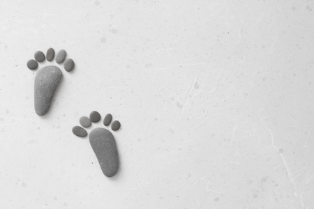Footprints made of stones. Happy feet. Stone arranged like footprints on the beach. Spa background with grey stones. Copy space for your text. Aromatherapy for beauty, relaxation, nature massage.の写真素材