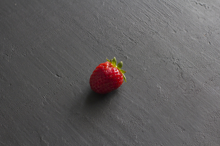 One red beautiful strawberry close-up, on a black dark concrete background. Minimalism. Side view, Copy Space For Your Text.の写真素材