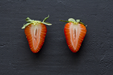 Two half strawberries, cut red beautiful strawberries close-up, on a black dark concrete background. Top View, Copy Space For Your Text. Fruit erotica.の写真素材
