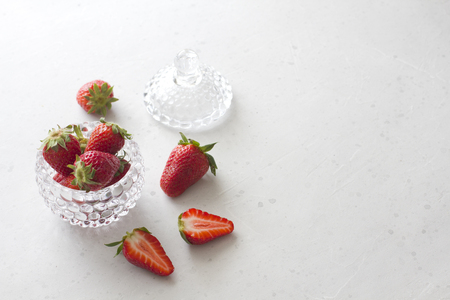 Beautiful red strawberry in glass round bowl. Strawberries on a light white concrete background. Rustic style. Cut strawberries, half. Horizontal. Top View, Copy Space For Your Text.の写真素材