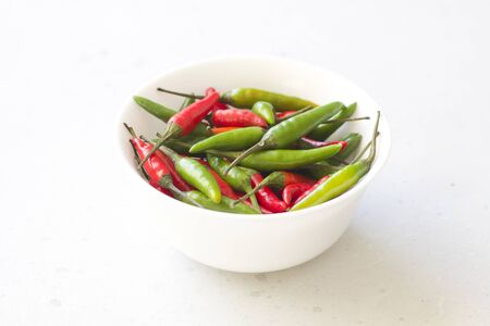 Red Hot Chili Peppers On Modern Background or White Table, on a Round Bowl. A Lot of Red Chilli Peppers. Green Hot Chili Peppers. Copy space for your text. Flat lay, top view. Colorful chili pepper.の写真素材
