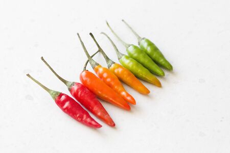 Red Hot Chili Peppers On Modern Background or White Table. A Lot of Red Chilli Peppers. Green Hot Chili Peppers. Copy space for your text. Flat lay, top view. Colorful chili pepper rainbow. Gradient.の写真素材