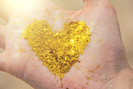 A golden shining heart lies in the hands of the girl. Golden heart.の写真素材