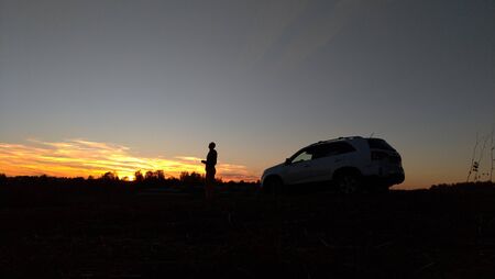 Black Silhouette of a plant, a man and a car on the background of a sunset and blue sky.
