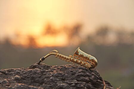 The golden alto saxophone lies on a black stone, against a background of sunset. Romantic musical background. Musical cover and creative. Design with copy space.の写真素材