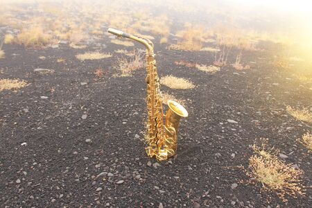 Golden Alto Saxophone Lies on the Black Background. Romantic and Beautiful Saxophone. Place for Text. The Etna volcano. The island of Sicily, Italy.の写真素材
