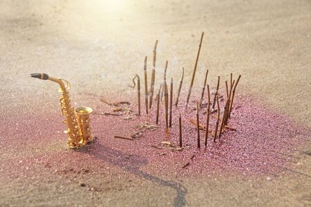 The golden saxophone alto stands on the sand next to the fragrant and pink shining. Romantic musical...