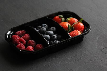 Fresh Sweet Berries strawberries, blueberries and raspberries lie in the tray, box on Black Background. Harvest Concept. Mix berries on a black background. Fruits with copy space for text.の写真素材
