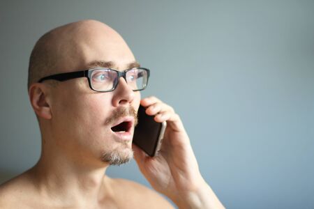 Young handsome man in black glasses is talking on the phone and is surprised. Closeup portrait of a man. Manager, office worker talking on the phone. Copy space for your text.の写真素材