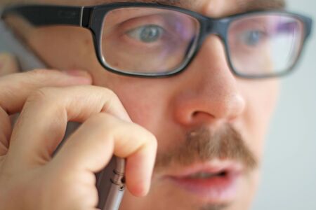 Young handsome man in black glasses is talking on the phone. Closeup portrait of a man. Manager, office worker, talking on the phone in emotions.の写真素材