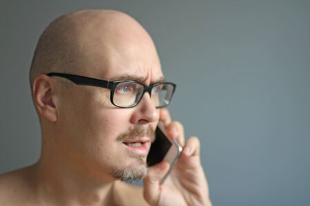 Young handsome man in black glasses is talking on the phone. Closeup portrait of a man. Manager, office worker, talking on the phone in emotions. Problems, bad deeds. Copy space for your text.の写真素材