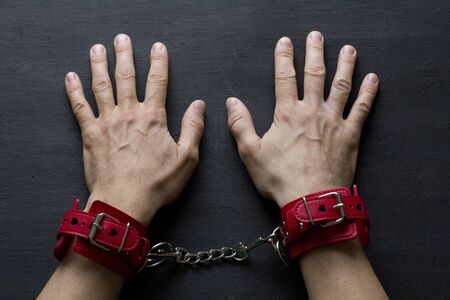 Adult male hands in red erotic leather handcuffs. Hands in captivity. Red leather handcuffs on black...