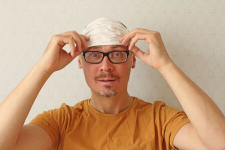 Young man incorrectly puts disposable protective white medical hygiene mask on his forehead to protect himself from respiratory, infectious viral diseases, from coronavirus. Humor, positive, fool.の写真素材