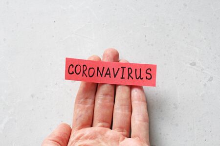 A hand holds the word Coronavirus, which is written on a red sheet of paper, on a light gray modern background. Epidemic, danger, recovery.の写真素材