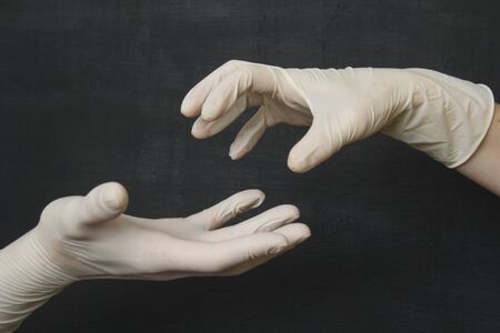 Hands in white latex rubber gloves on a black background. White medical gloves. Protective disposable gloves to protect against viruses, coronavirus and dangerous bacteria.の写真素材