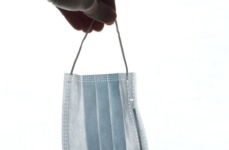 Blue medical mask. Surgical used mask with rubber ear straps. Typical 3-ply surgical mask to cover mouth, nose. Procedure mask from bacteria. Protection concept, against coronavirus. Hand holds mask.の写真素材