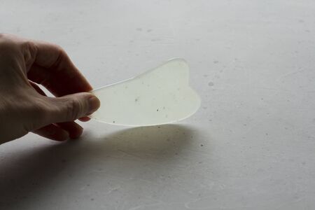 Young female hand holds gouacha scraper for massage of face, body, made from natural mineral white...
