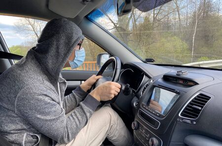 Man in medical protective mask driving car, close-up. Hygienic mask to prevent infection, airborne respiratory illness such as flu, Covid - 2019. Protection against coronavirus, contagious disease.の写真素材