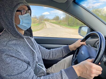 Man in medical protective mask driving car, close-up. Hygienic mask to prevent infection, airborne respiratory illness such as flu, Covid - 2019. Protection against coronavirus, contagious disease.の写真素材