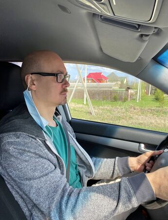Man in medical protective mask driving car, close-up. Hygienic mask to prevent infection, airborne respiratory illness such as flu, Covid - 2019. Protection against coronavirus, contagious disease.の写真素材