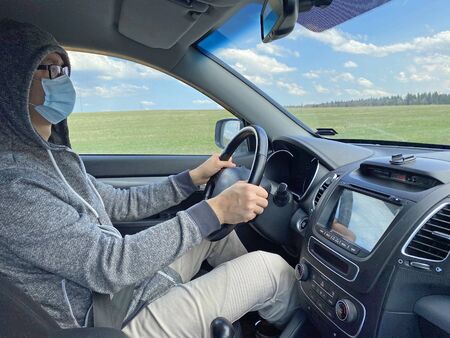 Man in medical protective mask driving car, close-up. Hygienic mask to prevent infection, airborne respiratory illness such as flu, Covid - 2019. Protection against coronavirus, contagious disease.の写真素材