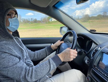 Man in medical protective mask driving car, close-up. Hygienic mask to prevent infection, airborne respiratory illness such as flu, Covid - 2019. Protection against coronavirus, contagious disease.の写真素材
