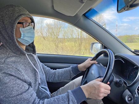 Man in medical protective mask driving car, close-up. Hygienic mask to prevent infection, airborne respiratory illness such as flu, Covid - 2019. Protection against coronavirus, contagious disease.の写真素材