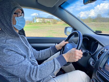 Man in medical protective mask driving car, close-up. Hygienic mask to prevent infection, airborne respiratory illness such as flu, Covid - 2019. Protection against coronavirus, contagious disease.の写真素材