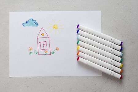 Drawn by colorful felt-tip pens a child's drawing on a white sheet of paper - a house, flowers, the...