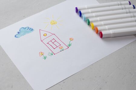Drawn by colorful felt-tip pens a child's drawing on a white sheet of paper - a house, flowers, the sun and cloud. Creativity, drawing for children, design. Many Markers of all colors of the rainbow.の写真素材