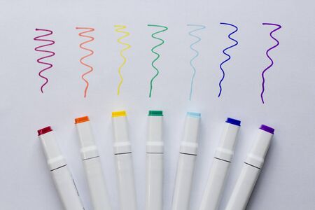 A set of bright multi-colored felt-tip pens or markers lie on white background sheet of paper, with samples of drawing. Creativity, drawing for children, design. Many Markers of all colors of rainbow.の写真素材