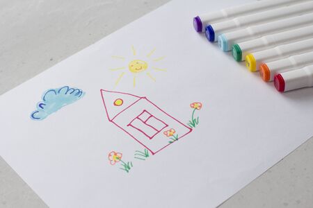 Drawn by colorful felt-tip pens a child's drawing on a white sheet of paper - a house, flowers, the sun and cloud. Creativity, drawing for children, design. Many Markers of all colors of the rainbow.の写真素材