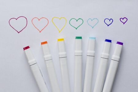 A set of bright multi-colored felt-tip pens or markers lie on a white background sheet of paper with painted hearts. Creativity, drawing for children, design. Many Markers of all colors of rainbow.の写真素材
