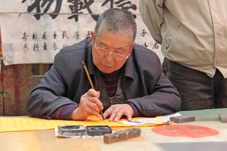 China, Suzhou - April 14, 2012. The man writes Chinese characters with a brush, calligraphy in China. The man is Chinese.のeditorial素材
