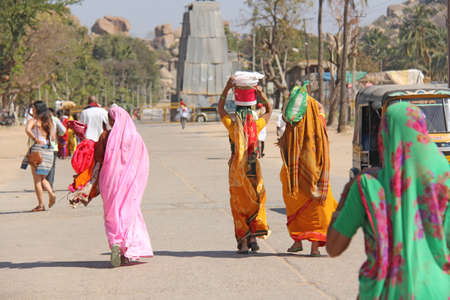 India. Hampi - February 1, 2018. A crowd of Indian men and women from the back in the saris on the streets of India. Bright colors of India. People of India and Hampi. Vijayanagar, karnataka, unesco.のeditorial素材