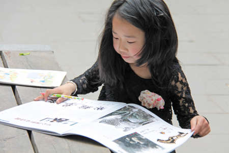 China, Suzhou - April 14, 2012. A Chinese girl draws in a book or paints pictures.のeditorial素材