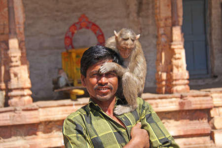 India, Hampi, 01 February 2018. The monkey sits on the shoulder of an Indian man. Close-up portrait.のeditorial素材