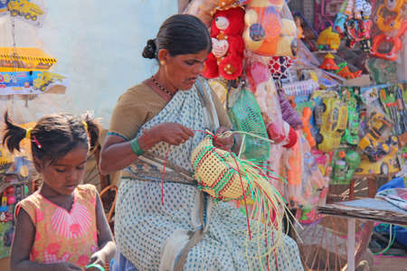 India, Hampi, 02 February 2018. A woman is engaged in needlework, weaves baskets of plastic. The saleswoman in the market. Trade in India.のeditorial素材